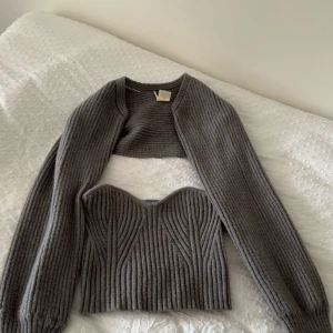 Grå stickad bolerotopp och korsett - Säljer en ribbstickad grå bolerotopp med långa ärmar och en matchande stickad korsett med snygg sweetheart-urringning. Setet har en cool struktur och är perfekt att styla med jeans eller kjol. Supermysigt material och trendig look.