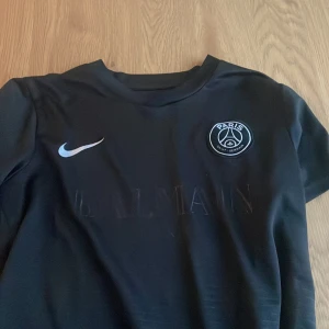 Svart PSG x Balmain fotbollströja Nike S - Svart Paris Saint-Germain fotbollströja i samarbete med Balmain, tillverkad i Nike Dri-Fit material. Tröjan har korta ärmar, rund hals och PSG-logga på bröstet samt Nike Swoosh. Diskret Balmain-tryck framtill och engineered-märke nedtill.