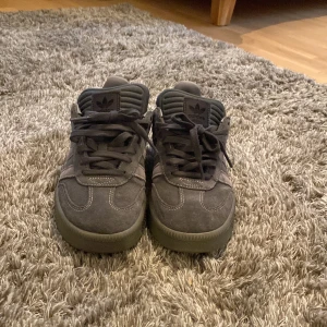 Adidas Samba grå mocka sneakers - Säljer ett par Adidas Samba sneakers i mörkgrå mocka med klassiska tre ränder på sidan och snörning framtill. Låg modell med rund tå och platt sula. Storlek 42.