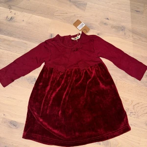 Vinröd sammetsklänning med rosett 🎁 julklänning  - Supersöt vinröd klänning från Mini Rodini med långärmade ärmar och sammetskjol. Klänningen har en fin rosettdetalj framtill och tryckknappar i nacken för enkel påklädning. Perfekt för dig som vill ha något gulligt och stilrent till de små. Fungerar perfekt till alla tillfällen som julafton, sommar, födelsedagar 🎉 