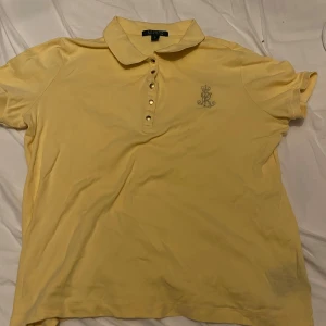 Gul pikétröja från Ralph Lauren XL - Snygg gul pikétröja från Ralph Lauren i storlek XL. Tröjan har klassisk krage, knappar framtill och broderad logga på bröstet. Tillverkad i mjuk bomull, perfekt för vår och sommar. Enkel att matcha med jeans eller shorts.