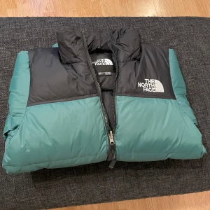 Grön och svart pufferjacka North Face - Säljer denna originala The North Face Retro Nuptse-jacka. Jag köpte den men den är alldeles för liten för mig, så jag har bara provat den en gång. Den är som ny, utan fläckar eller slitage. Storlek: XS  Fraktalternativ (från Norge): – Posten / Bring – Helthjem – PostNord Norge 