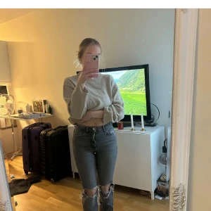 Gråa jeans  - Säljer ett par gråa jeans med hög midja och stora slitningar över knäna. Jeansen har klassisk femficksdesign, raka ben och är i ett stretchigt denimtyg. Perfekta för en avslappnad och trendig look.