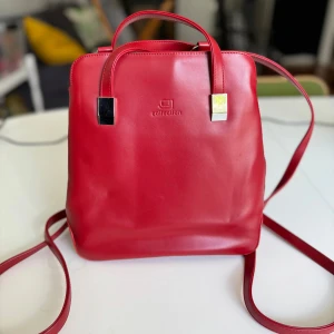 Röd ryggsäck från Collection ❤️ - Snygg röd väska i nyskick från Collection. Kan användas som axelremsväska eller ryggsäck. Väskan är i syntet och har en stilren design med silverdetaljer. Dragkedja på baksidan och justerbara axelremmar. 24x23cm. Hämtas på Hägerstensåsen eller ök ❤️🍎❤️ 