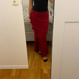 Maxi kjol  - Säljer min helt oanvända mörkröda maxi kjol från Na-Kd gamla kollektion. Med massor av snygga volanger och en slits slängs benet. Kjolen är tunn och är väldigt stretchig vid midjan.