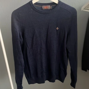 Mörkblå merinoullströja från Morris - Snygg mörkblå stickad tröja från Morris i 100% merinoull. Klassisk rund halsringning och diskret logga broderad på bröstet. Perfekt för dig som gillar stilrena och bekväma plagg med premiumkänsla.