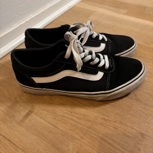 Svarta Vans sneakers strl 40 - Klassiska Vans Old Skool sneakers i svart med vit sidorand och vita snören. Skorna har platt sula, rund tå och är tillverkade i en mix av mocka och canvas. Perfekta för en avslappnad streetstyle-look.
