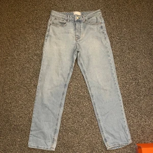 Ljusblå jeans från ASOS - Ljusblå jeans från ASOS DESIGN med hög midja och raka ben. Klassisk femficksmodell med dragkedja och knapp framtill. Jeansen är tillverkade i bomull och har en avslappnad, straight fit som passar till allt.