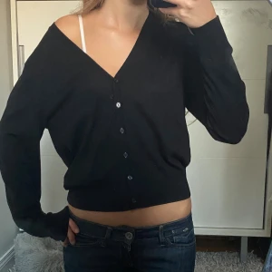 Svart kofta i 100% merinoull med knappar - Säljer denna Svarta kofta med v-ringning och knappar framtill. Modellen är lite loose och har långa ärmar. Perfekt att bära offshoulder vilket jag tycker är supersnyggt. Passar till allt och är perfekt nu till hösten. Den är i 100% merinoull från Lindex i storlek M men passar mig som brukar ha xs/s.