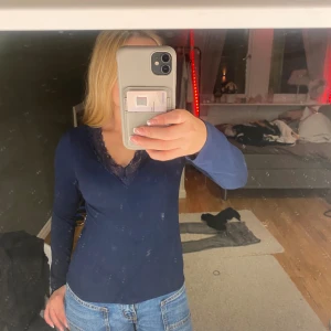 Mörkblå långärmad topp med spets - Mörkblå långärmad topp med v-ringning och snygg spetskant runt halsen. Toppens material är mjukt och stretchigt, perfekt till jeans eller kjol. Enkel men ändå med en fin detalj som gör den lite extra.