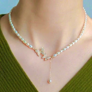 Pärlhalsband med fjärilar och kedja - Superfint halsband med vita pärlor och tre glittriga fjärilar i guld. En tunn guldkedja med en pärla hänger ner från ena sidan för extra detalj. Perfekt för dig som gillar söta och eleganta smycken med lite extra bling.