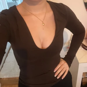 Brun långärmad body med v-ringning - Säljer en brun långärmad body med v-ringning. Toppen har en tight passform och är tillverkad i ett mjukt, stretchigt material som sitter snyggt på kroppen🩷. Köpt på hm för 2 år sedan, aldrig använd🩷
