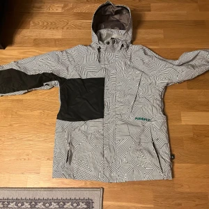 Mönstrad vinterjacka från Firefly - Säljer en snygg vinterjacka från Firefly med svartvitt grafiskt mönster och svarta detaljer på ärm och bröst. Jackan har huva med snörning, dragkedja och praktiska fickor. Insidan är gul med stor Firefly-logga. Perfekt för dig som vill sticka ut i höst och vinter.