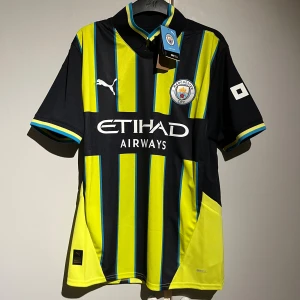 Manchester City bortatröja Puma M - Manchester City bortatröja från Puma i mörkblå och gul med blå detaljer. Tröjan har korta ärmar, randigt mönster och klubbmärke på bröstet. Tillverkad i lätt och ventilerande polyester med Etihad Airways-tryck på framsidan.