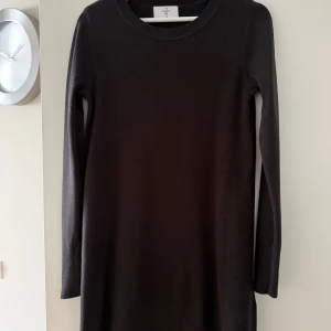 C&A svart stickad klänning, storlek S - -Svart klänning med långa ärmar och dekorativa guldknappar på ärmsluten.  -Klänningen har en enkel, rund halsringning och en rak passform. -85 cm lång -Mycket bra skick  Djur och rökfritt hem