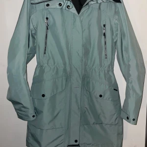 Ljusgrön parkajacka från Everest - Snygg TCS waterproof parkajacka från Everest med huva, dragkedja och knappar framtill. Jackan har två stora fickor med lock och två bröstfickor med dragkedja. Perfekt längd och stilren design, tillverkad i slitstark polyester.