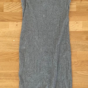Grå ribbad ärmlös klänning från Bershka - Säljer en grå, ribbad klänning från Bershka i storlek S. Klänningen är ärmlös med hög hals och har en tight passform som framhäver siluetten. Perfekt för dig som gillar minimalistisk stil och vill ha något enkelt men snyggt.