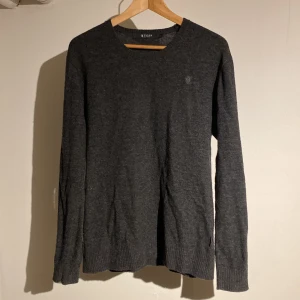 Mörkgrå stickad tröja Tiger of Sweden - Mörkgrå stickad tröja från Tiger of Sweden i klassisk modell med rund halsringning. Tröjan har ribbade muddar vid ärmslut och nederkant, och är tillverkad i mjukt material som passar perfekt till lager-på-lager. Enkel och stilren design. Den är lite nopprig men går lätt och ta bort! Hör av dig vid minsta fundering!