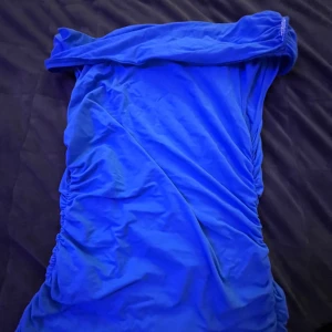 Blå offshoulder kortklänning - Snygg blå t-shirt med offshoulder-design och rynkade sidor. Klänningen har en tight passform och är perfekt för dig som vill sticka ut. Tillverkad i ett mjukt och stretchigt material som sitter bekvämt på kroppen.💙