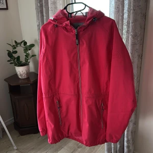 Röd vindjacka från McKinley - Säljer en röd vindjacka från McKinley med huva och dragkedja framtill. Jackan har två fickor med dragkedja, elastiska muddar och meshfoder i huvan. Perfekt för dig som gillar sportig stil och vill ha något lätt och funktionellt.