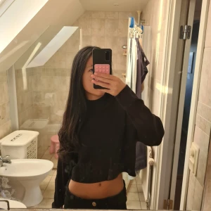 Svart croppad stickad tröja - Säljer en svart croppad stickad tröja med ribbad hög hals och långa ärmar. Tröjan har en loose passform och är perfekt att styla med höga jeans eller kjol. Enkel och stilren design som funkar till många olika looks.