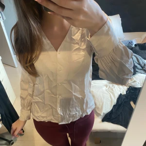 Beige blus med v-ringning och knappar - Snygg beige blus med v-ringad hals och knappar. Långa ärmar med knappar.