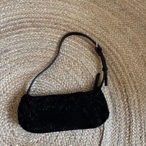 Svart glittrig axelväska med dragkedja - En svart axelväska från Lindex med glittriga detaljer och justerbart axelband i skinn. Väskan har en silverfärgad dragkedja upptill och en mjuk, avlång form. Perfekt för dig som vill ha en snygg och trendig accessoar med lite extra bling. Väskan har använts max 2 gånger. Pris kan diskuteras 💗
