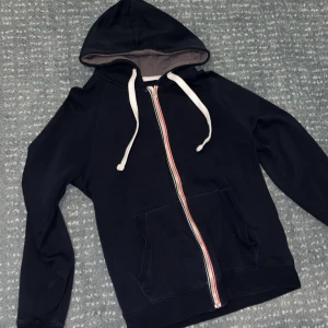 Mörkblå hoodie S - Mörkblå hoodie från Pier One med vit dragsko och hel dragkedja med röd och vit detalj. Tröjan har känguruficka framtill och mjukt grått foder i huvan. Perfekt för chill dagar eller när du vill ha en enkel och snygg look.