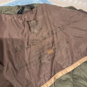 Grön quiltad jacka Hansen & Jacob S - Snygg quiltad jacka från Hansen & Jacob i storlek S. Jackan är grön med bruna och beige detaljer, har dragkedja och innerficka med dragkedja. Stort broderat H&J-logo på insidan och exklusiv känsla i materialet. Perfekt för dig som gillar stilrena och klassiska plagg. Ny pris 3,700 