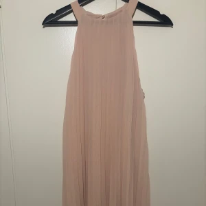  klänning - Superfin plisserad klänning ärmlös design. Klänningen har hög halsringning och knäpps med en liten knapp i nacken. 