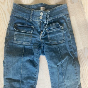 Blå jeans med fickor och hög midja - Snygga blå jeans från NLY med hög midja, dubbla knappar och dragkedja. Byxorna har raka ben och två stora fickor framtill som ger en cool look. Perfekta för dig som gillar en trendig och bekväm stil.
