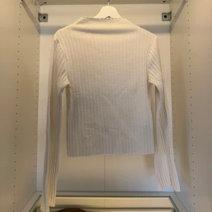 Vit ribbad långärmad tröja - Säljer en vit ribbad långärmad tröja med smal passform och hög hals. Tröjan är stickad i ett mjukt material och har en clean, minimalistisk look som passar perfekt till jeans eller kjol.