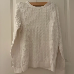 Vit kabelstickad tröja - Säljer en klassisk vit kabelstickad tröja med rund hals och långa ärmar. Tröjan har ett snyggt flätmönster över hela och ribbade muddar vid ärmslut och nederkant. Perfekt för lager-på-lager och en clean look. Jätte fin vit tröja Använd ett fåtal gånger  Köptes för 250 Säljer för 150 pris kan diskuteras