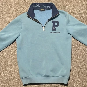 Blå half zip tröja Polo Ralph Lauren  - Säljer en ljusblå långärmad tröja från Polo Ralph Lauren med half zip och hög krage. Tröjan har broderad logga och stort P på bröstet samt mjukt fleecefoder på insidan. Perfekt för dig som gillar klassisk och sportig stil. Storlek S