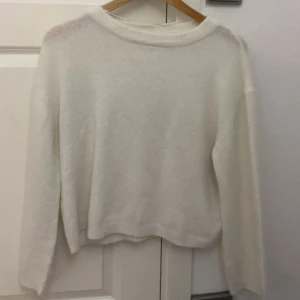 Vit stickad tröja med rund hals - Mysig vit stickad tröja med rund halsringning och långa ärmar. Tröjan har en enkel och stilren design med ribbade muddar vid hals, ärmslut och nederkant. Perfekt för lager-på-lager under kyliga dagar.