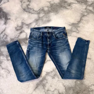 Replay Anbass slim fit jeans blå - Säljer ett par Replay Anbass jeans i klassisk blå tvätt med snygga slitningar. Modellen är skinny med smal passform och normal midja. Jeansen har fem fickor, dragkedja och är tillverkade i stretchig bomull för extra komfort. (SMÅ DEFEKTER SOM GÅR OCH FIXA).
