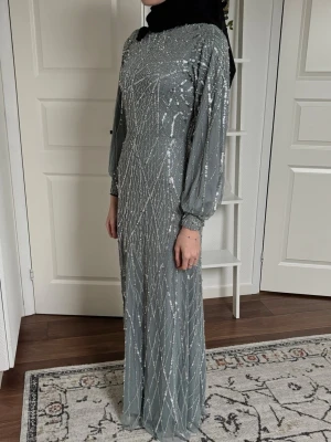 Glittrig långklänning i silvergrått - Nypris 3000kr - Mycket elegant långklänning/maxiklänning i en mjuk grågrön/salviagrön ton med vackert silverglittrande mönster över hela klänningen. Perfekt för fest, bröllop, eid, förlovning eller andra högtidliga tillfällen. Använd 1 gång i endast ett par timmar - klänningen är som ny. #maxiklänning #långklänning #festklänning #modestfashion #modestwear #hijabstyle #muslimfashion #elegantklänning #glitterklänning #silverglitter 