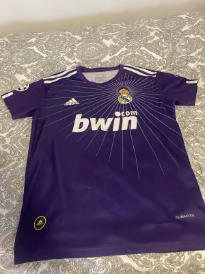 Lila Real Madrid Ronaldo tröja Adidas - Säljer en lila Real Madrid matchtröja från Adidas med Ronaldo och nummer 7 på ryggen. Tröjan har vita detaljer, Champions League-märke på ärmen och ett coolt strålande mönster från klubbmärket. Materialet är lätt polyester med ClimaCool-teknologi.