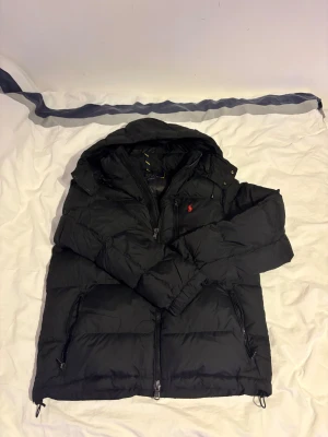 Ralph Lauren jacka - Hej, säljer nu min gamla Ralph lauren pufferjacka pågrund av ny jacka själv! Den är använd typ en och en halv vinter men är fortfarande i riktigt bra skick! Ända är ett dunet blivit lite slitet och så men inget överdrivet som du kan se på bilderna. Storlek M och passar mig på 1,80 perfekt. Tveka ej skicka ett prisförslag eller skicka iväg en fråga!