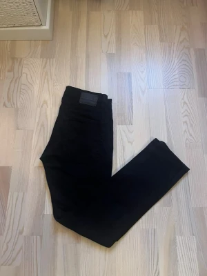 Svarta jeansbyxor från 157, W30 L32 / M - Svarta jeansbyxor från 157 i klassisk femficksmodell. Byxorna har en rak passform med normal midja och är tillverkade i ett mjukt bomullsmaterial med lite stretch. Snygga nitar vid fickorna och stilren design utan synliga mönster eller detaljer. W30 L32