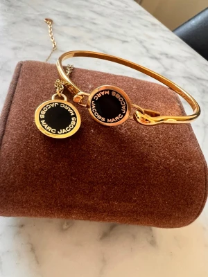 MJ remand och halsband  - Bilderna visar ett armband och ett halsband från Marc Jacobs i guld och svart, men ingen väst syns.