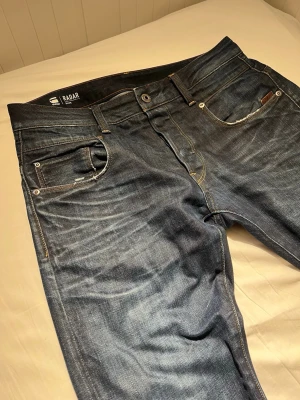 G-Star RAW jeans blå - Säljer ett par G-Star RAW Radar Slim jeans i mörkblå tvätt med snygga slitningar och kontrastsömmar. Perfekt för dig som gillar stilrena och moderna jeans med lite edge. Midja: 41 cm. Längd: 97 cm. Tveka inte att skriva om du har frågor🤙