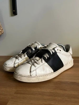 Valentino Open sneakers vit/svart - Tjena, jag säljer ett par svarta Valentino open. Skorna är använda varsamt men finns såklart tecken på användning, men dem gör fortfarande sin grej genom att vara stiliga och sköna. Dem är 100% äkta men finns inte kvitto eller kartong för att jag köpte dem av en kompis för cirka 6 månader sedan. Jag säljer dem på grund av att jag skaffat nya skor och har då ingen användning av dessa😊 Jag gjorde mitt bästa när jag snörade om dessa men som ni ser gick det inte så galant hehe. Lägg gärna ett bud😊