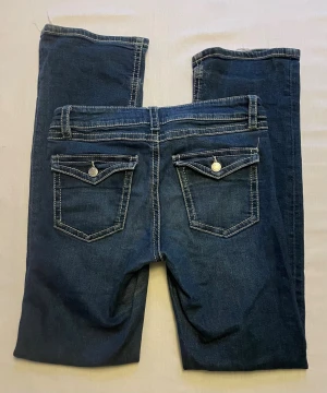 Gina tricot Mörkblå jeans  - Snygga mörkblå jeans från Gina tricot med vita kontrastsömmar och dekorativa ficklock med knappar bak. Klassisk femficksmodell och låg midja. 