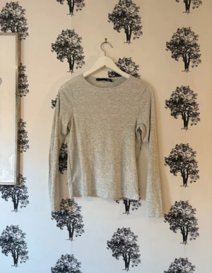Ljusgrå långärmad topp  - Säljer en enkel och stilren ljusgrå långärmad topp från Lager 157. Toppen har rund halsringning och är tillverkad i mjuk bomull med diskret ribbad struktur. Perfekt att matcha med jeans eller kjol för en clean look.