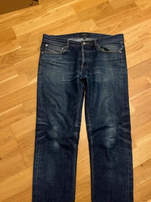 Selvedge A.P.C. Petit New Standard jeans blå - Snygga blå jeans från A.P.C. Petit New Standard med klassisk femficksdesign och raka ben. Jeansen har subtila slitningar och kontrastsömmar, samt en knappgylf. Perfekt passform för dig som gillar stilrena och tidlösa jeans. Finns ett litet hål på vänster ficka men inget som varken syns eller märks vid användning. W29