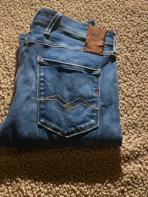 Replay Hyperflex blå jeans - Säljer ett par Replay Hyperflex jeans i klassisk blå färg med snygga kontrastsömmar och detaljerade bakfickor. Jeansen har en modern passform och är tillverkade i stretchigt jeansmaterial som ger extra komfort. Perfekt för dig som gillar stilrena och coola jeans.