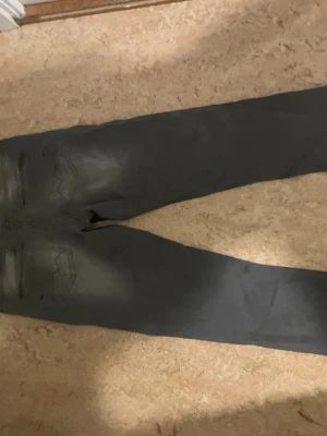 Replay grå jeans med tapered fit - Säljer ett par grå jeans från Replay med snyggt tvättad look och klassiska fem fickor. Modellen har tapered fit och normal passform, med subtila slitningar och Replay-logga på bakfickan. Perfekt för dig som gillar stilrena och bekväma jeans.