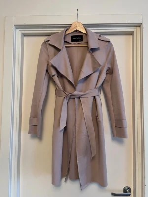 Dimrosa trenchcoat - Elegant trenchcoat i mjuk och skön borstad mocka. Storlek XXS men passar XS-S också. Använd en gång. Färgen är en ljus dimrosa. 