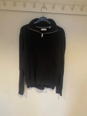 Svart stickad tröja från Jack & Jones - Säljer en svart stickad tröja från Jack & Jones med hög krage och half zip-dragkedja. Tröjan har lång ärm och en clean, enkel design som passar perfekt till höst och vinter. Skön och stilren för dig som gillar basic men ändå vill ha något extra.